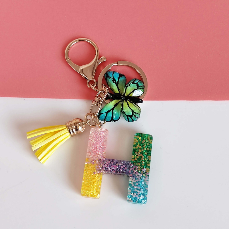 Ristäärisega 26 initsiaali vikerkaare järkjärgulise tutiga liblika ripatsiga võtmehoidja, litritega liimvaigust võtmehoidja