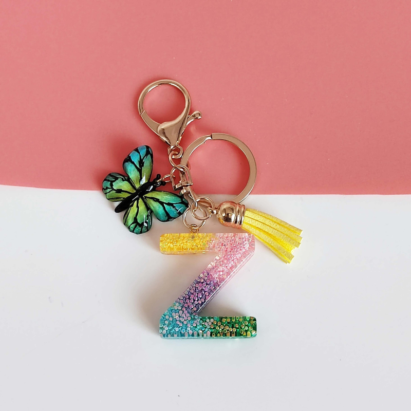 Ristäärisega 26 initsiaali vikerkaare järkjärgulise tutiga liblika ripatsiga võtmehoidja, litritega liimvaigust võtmehoidja