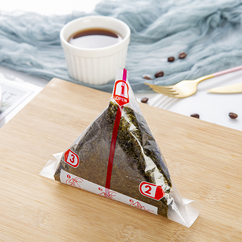 Dvisluoksnis trikampis ryžių kamuoliukų pakavimo maišelis, pusiau supjaustyti jūros dumbliai, rankomis susukta suši pakuotė, lengvai plyštanti ir nerasojanti, japoniško stiliaus jūros dumbliais apvyniota akmens masė