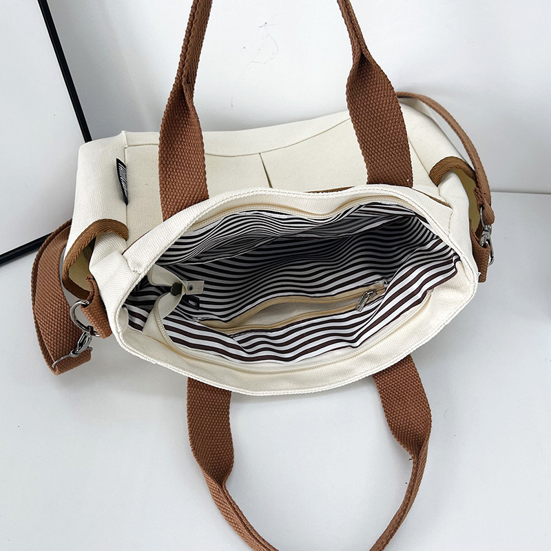 Geantă tote din pânză, cu stil urban minimalist, formă orizontală pătrată, închidere cu fermoar, buzunar pentru ID, trei curele de umăr și căptușeală poliester-bumbac.