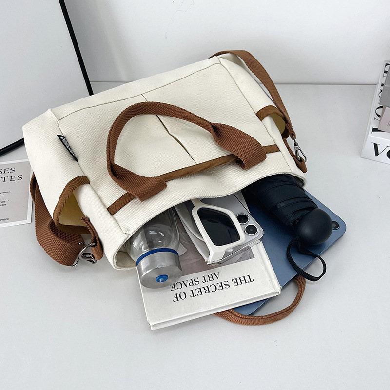 Geantă tote din pânză, cu stil urban minimalist, formă orizontală pătrată, închidere cu fermoar, buzunar pentru ID, trei curele de umăr și căptușeală poliester-bumbac.