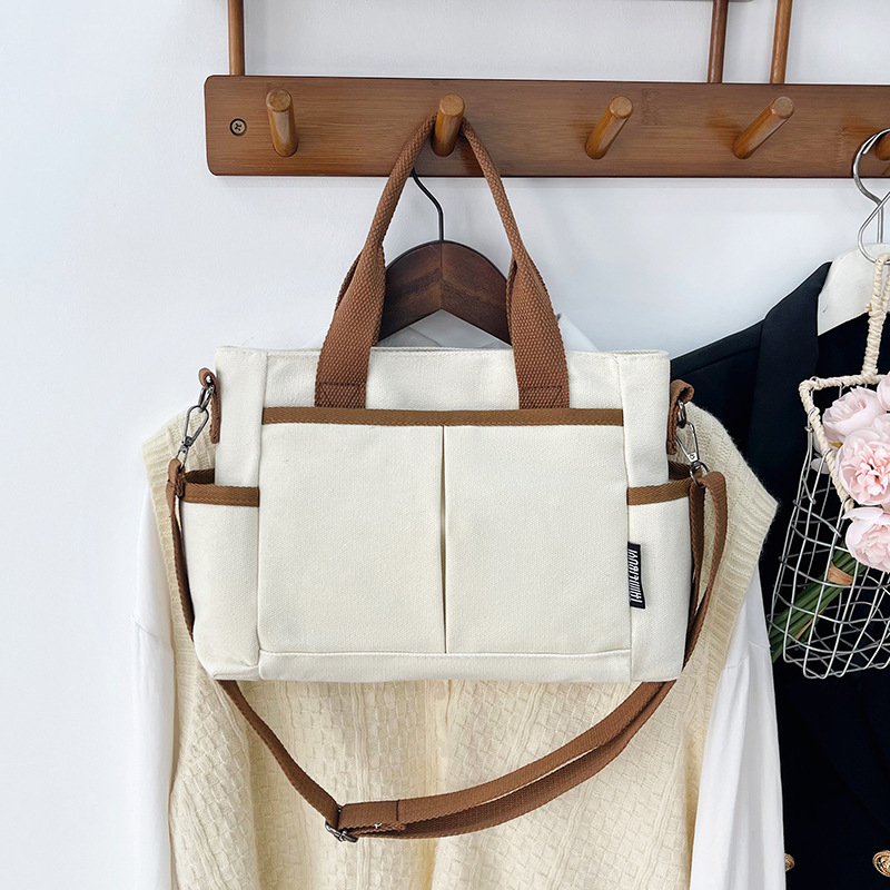 Geantă tote din pânză, cu stil urban minimalist, formă orizontală pătrată, închidere cu fermoar, buzunar pentru ID, trei curele de umăr și căptușeală poliester-bumbac.