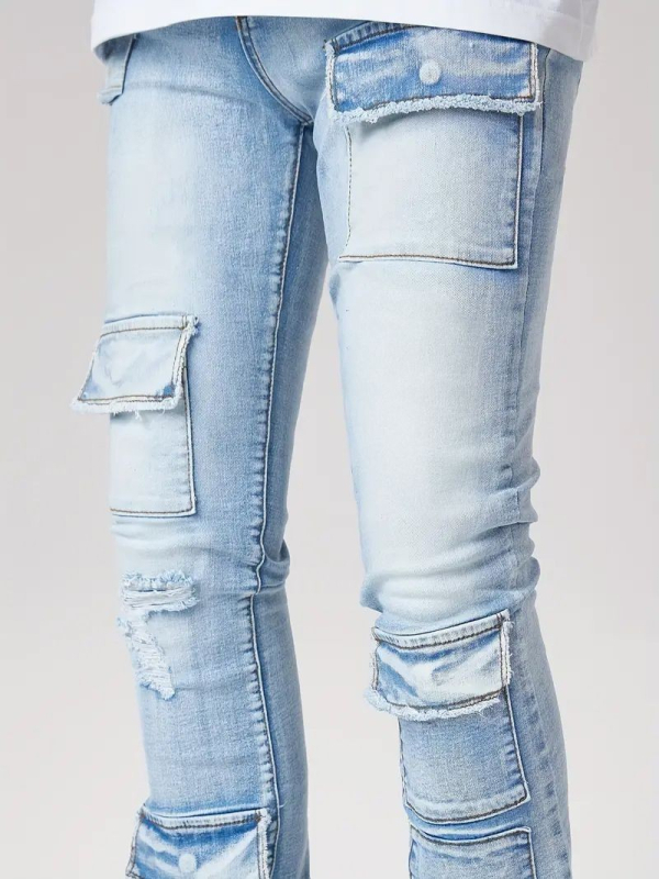 Džinsai gatvės stiliuje su keliomis kišenėmis, šiek tiek platėjantis kelnių galas, vidutinio aukščio juosmuo, užtrauktukas