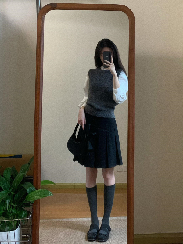 Trojdielny kostým: pletený vest, vrstvená košeľa a vysokopásová A-linijová plisovaná sukňa; jednofarebný vzor, stredná dĺžka sukne, retro štýl