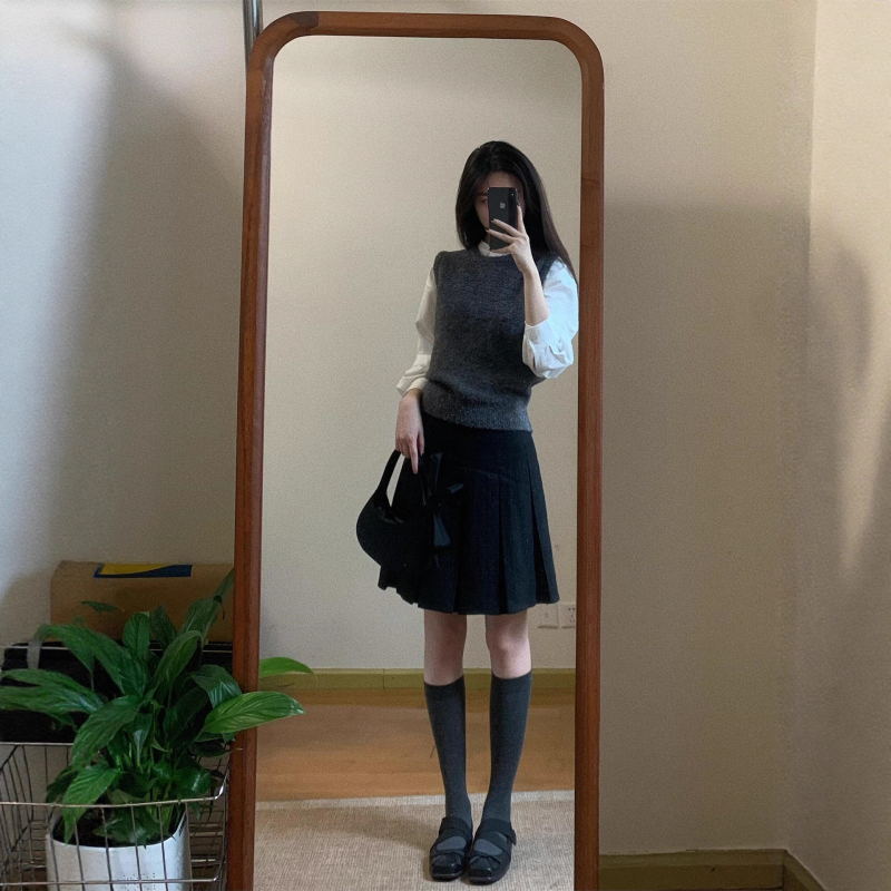 Trojdielny kostým: pletený vest, vrstvená košeľa a vysokopásová A-linijová plisovaná sukňa; jednofarebný vzor, stredná dĺžka sukne, retro štýl