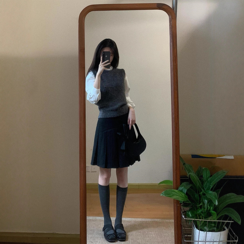 Trojdielny kostým: pletený vest, vrstvená košeľa a vysokopásová A-linijová plisovaná sukňa; jednofarebný vzor, stredná dĺžka sukne, retro štýl